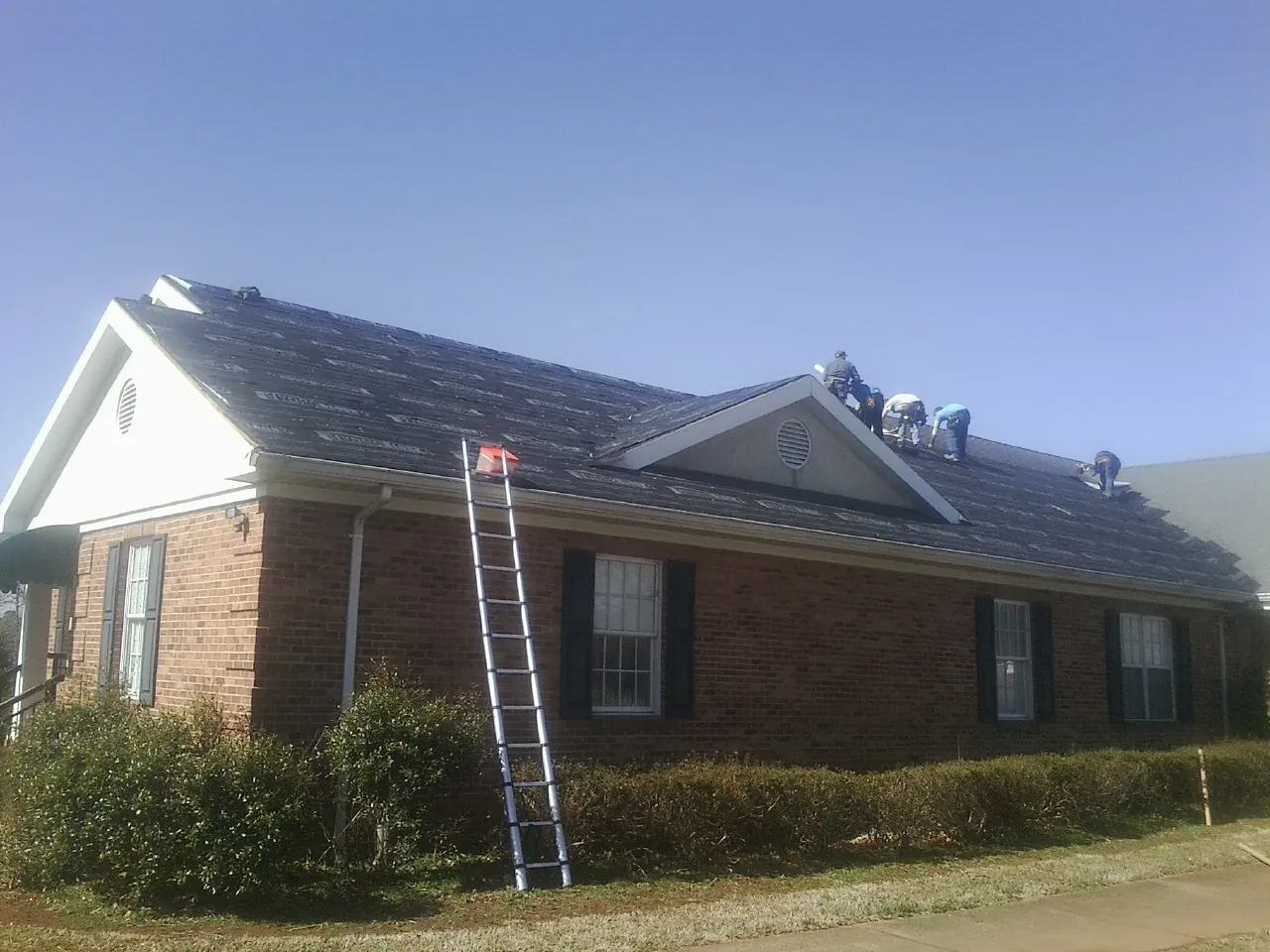 Crew tearing shingles off a brick ranch roof with a ladder set — Metal Roof Repair work by our crew in Liverpool