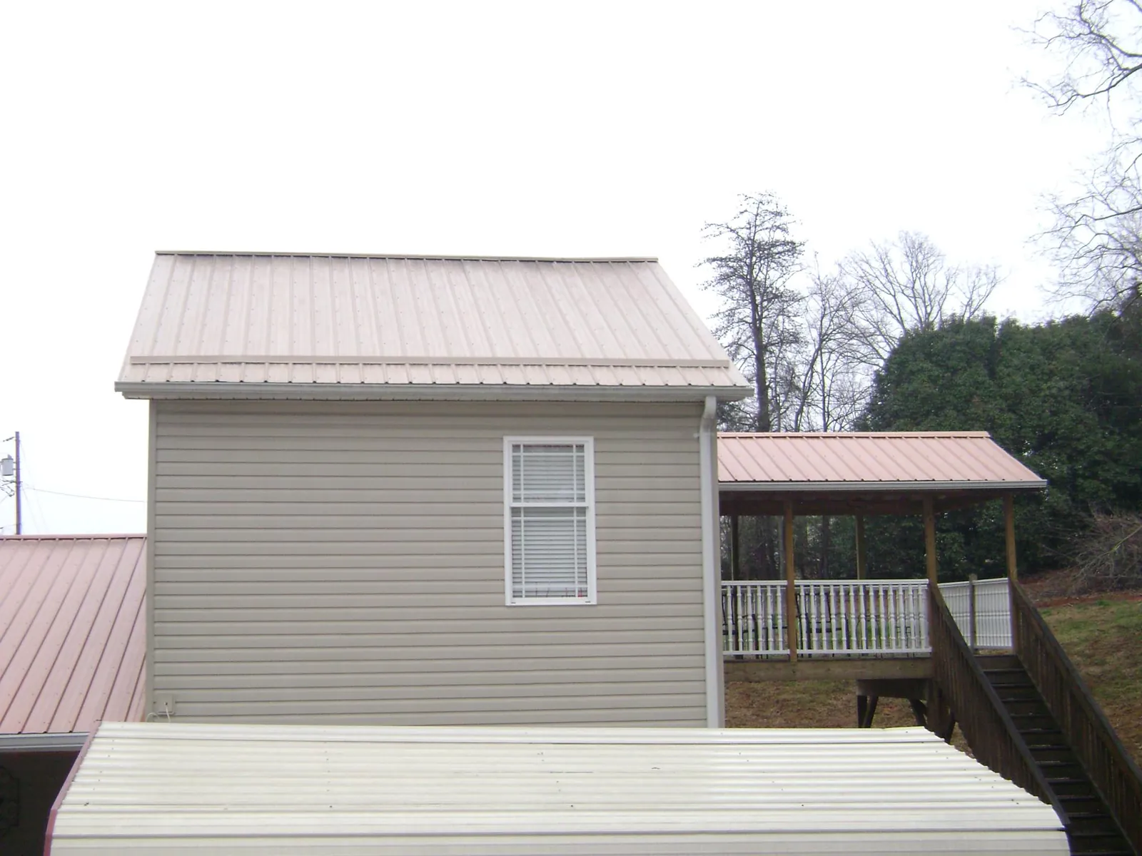 Tan metal roofs on a two story addition and attached porch, from a Roof Replacement job in Liverpool